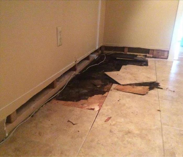 Room with tile floor busted up to reveal water damage to subfloor