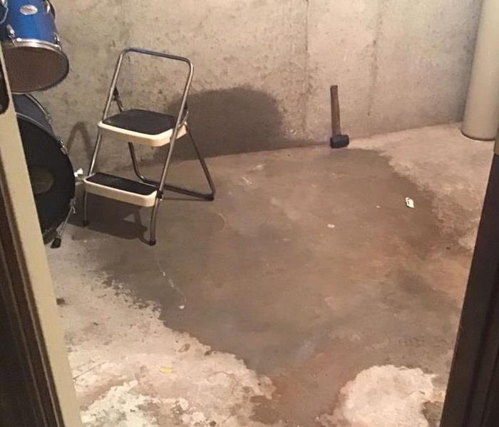 Basement with concrete wall and floor with water damage and a blue drum set on the floor