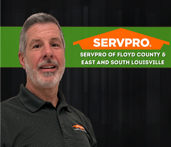 man looking at camera with a SERVPRO shirt on and a SERVPRO logo behind him on a black background