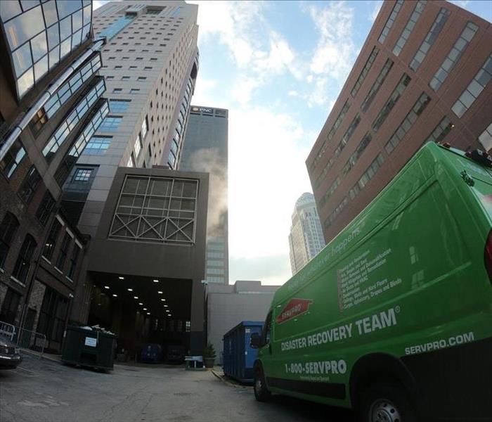 Green SERVPRO van parked in front of tall buildings in downtown Louisville.  There are two dumpsters nearby.