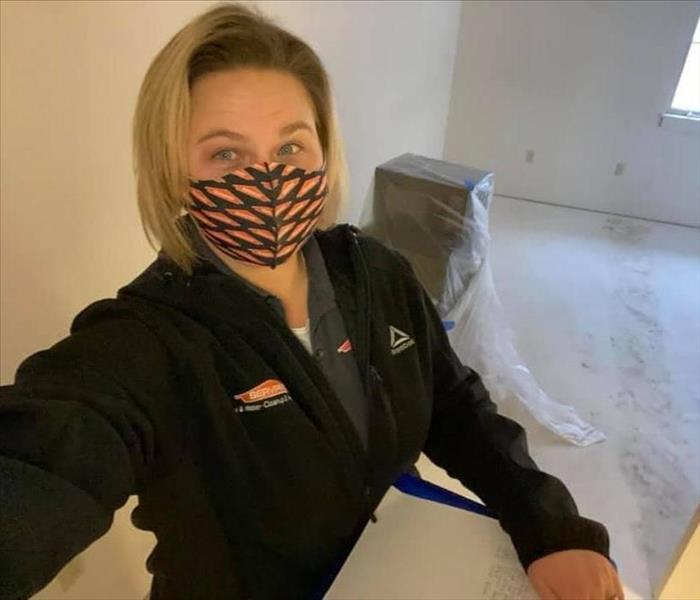 Woman with short blond hair wearing a black jacket and SERVPRO orange and black facemask standing in a demoed room
