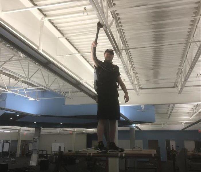 Man standing on scaffolding using a HEPA vacuum cleaner to clean a metal ceiling in a commercial warehouse 