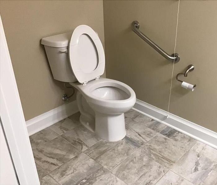 Bathroom with grey flooring, tan walls, white toilet with lid open.