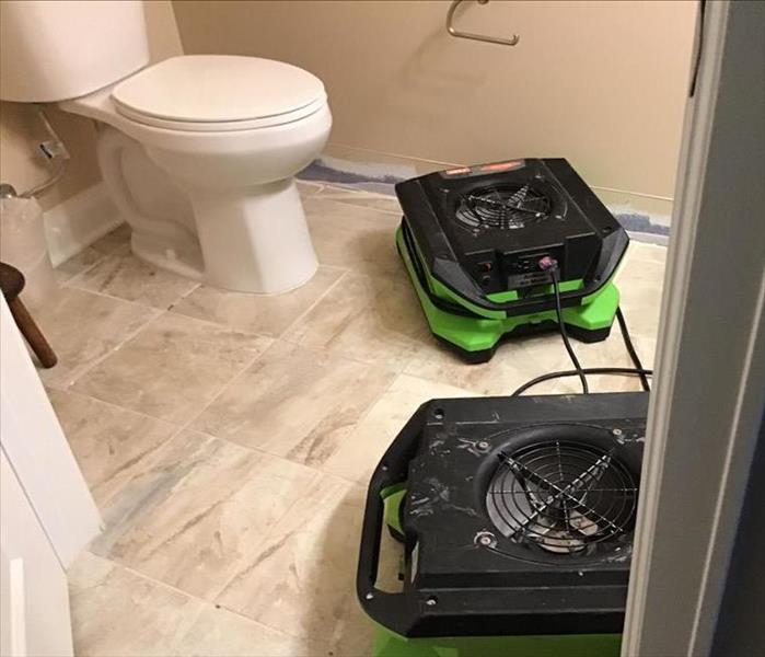 Bathroom with water damage.  Two fans set up on floor and baseboard removed from one wall.
